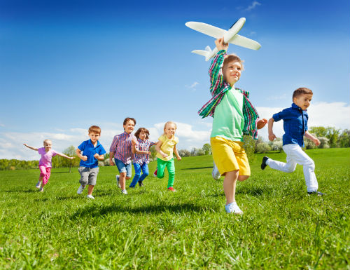 children running in a field with one holding up a toy aeroplane