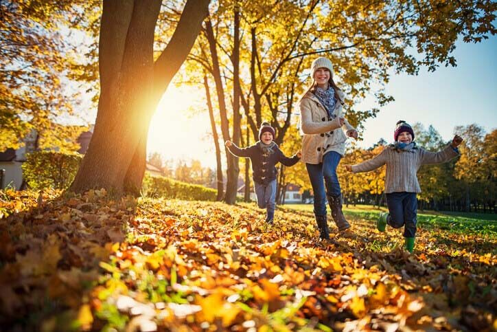 Three children of varying ages running through autumn leaves